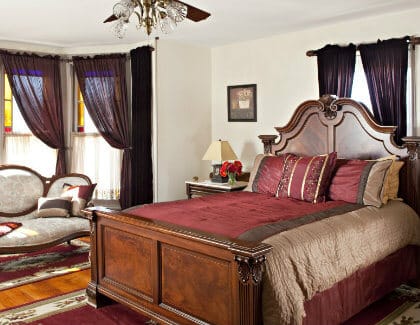 Elegant ivory guest room with carved wood bed, several windows and an antique love seat