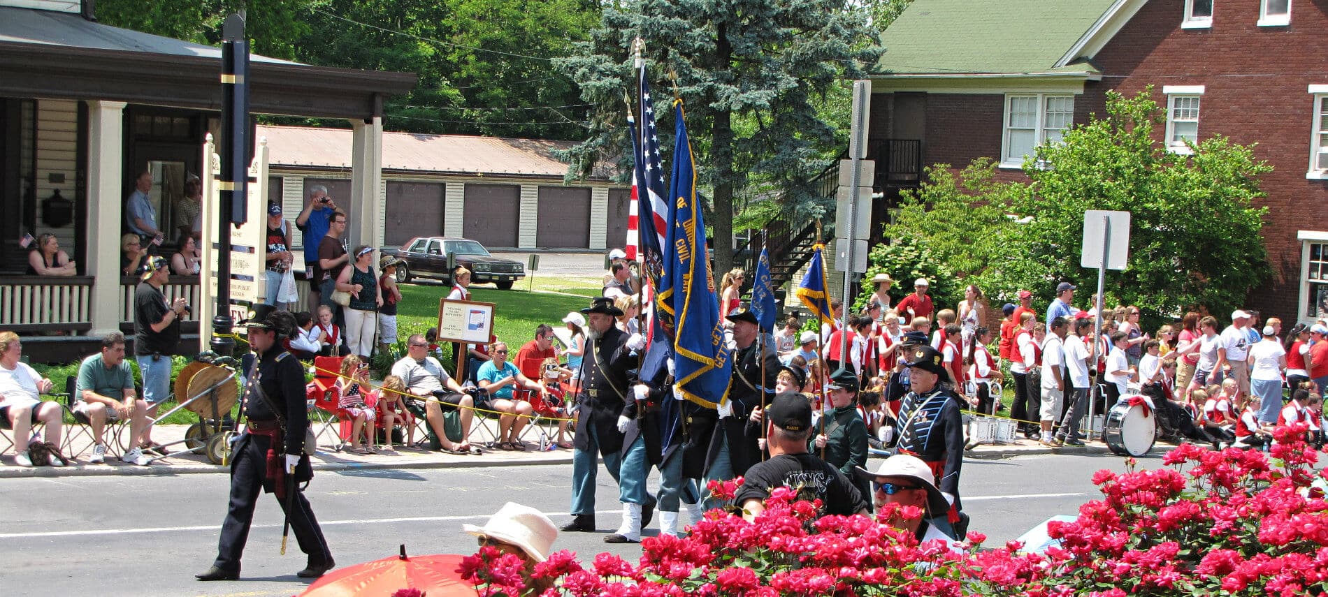 Armed forces in their uniforms walking down the crowd-lined street carrying flags during a city festival